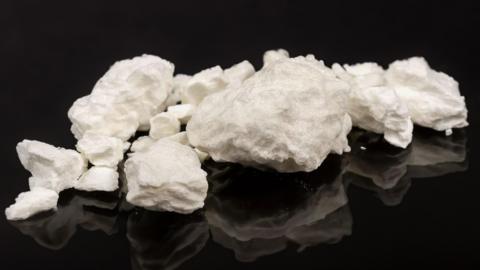 An image of crack cocaine - a white rock/rubble shaped drug laid out on a black table 