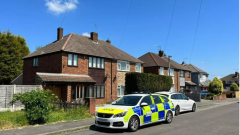 A police car parked outside of a semi-detached property on a residential street