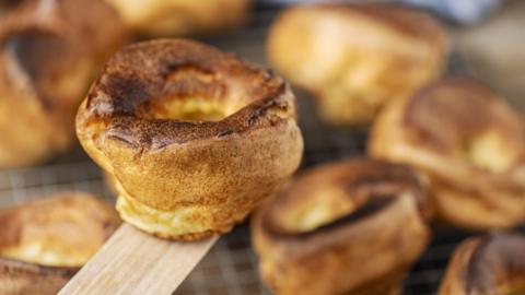A crispy golden Yorkshire pudding is lifted up by a wooden spatula 