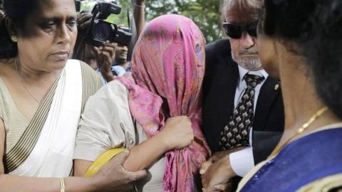 The employee of the Swiss embassy in Sri Lanka (head covered) is escorted by a police officer in Colombo on 16 December 2019