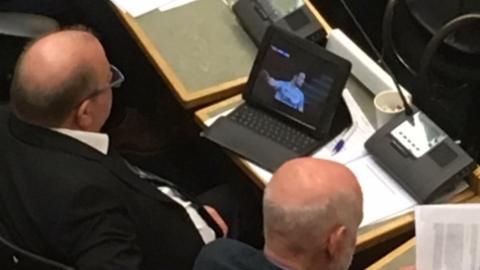 Kirklees Labour councillor Steve Hall watching a football match during a council debate in Huddersfield Town Hall.
