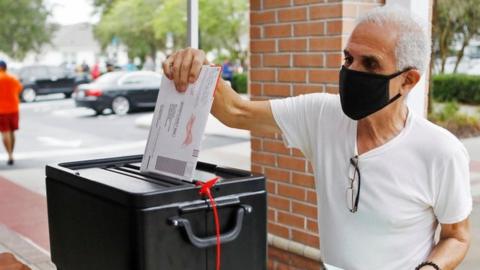 Man in a black face mask returns his mail-in ballot