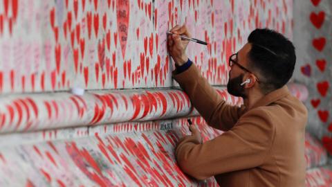 A man writes on the wall of the Covid memorial