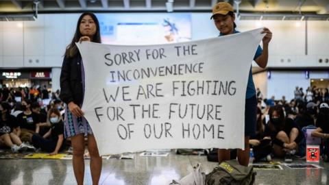 Hong Kong activists at an airport rally hold a banner reading: "Sorry for the inconvenience we are fighting for the future of our home", 9 August 2019