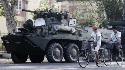 People cycle past armoured vehicles stationed in front of the Central Women Hospital in Yangon, Myanmar, 15 February 2021.