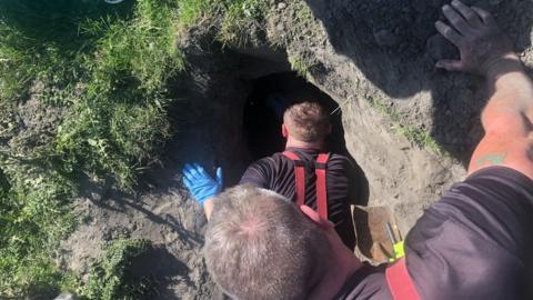 Firefighters getting to a dog down a hole