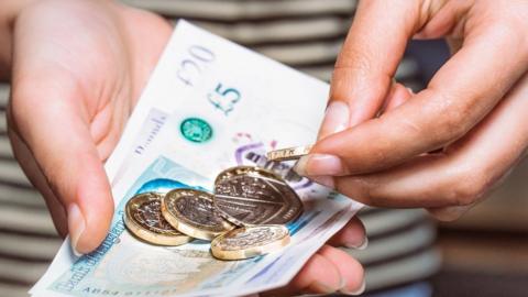 Man holding £5 note and pound coins