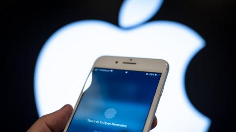 An iPhone locked awaiting a thumbprint is seen in front of a glowing Apple logo in the background