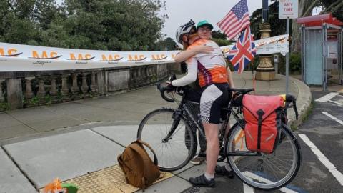 A cyclist hugging a woman next to a finish line banner