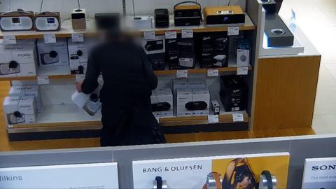man standing an electronics counter picking up a speaker