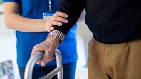 nurse helps elderly man holding frame