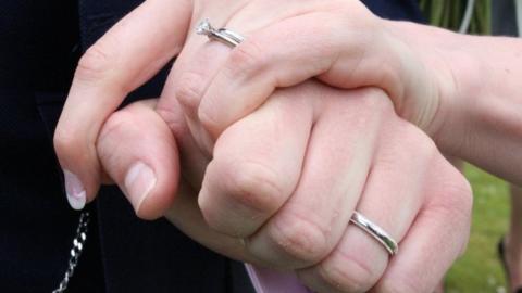Two people holding hands with wedding rings on