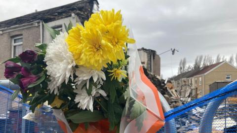Flowers in a barrier fence outside a devastated terrance home