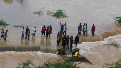 An aerial view from a helicopter shows people displaced by flood waters following heavy rains gather along a broken road in Hola, Kenya