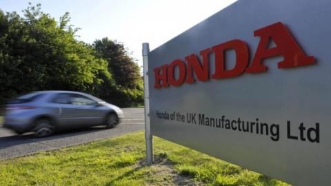 Honda car drives past sign for factory