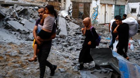 Palestinians carry their belongings as they walk on a debris-strewn street in the aftermath of Israeli strikes, following a Hamas surprise attack, at Beach refugee camp, in Gaza City, October 9, 2023