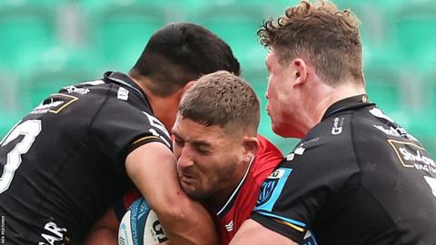 Munster's Dan Goggin is tackled by Sio Tomkinson and Will Rowlands of Dragons