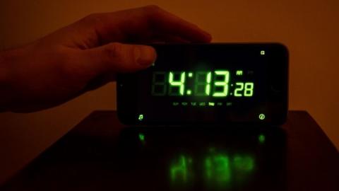 A man reaches over a digital clock