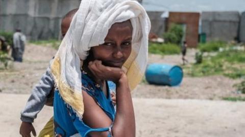 A woman holds a baby as she rests over a sack of wheat during a food distribution