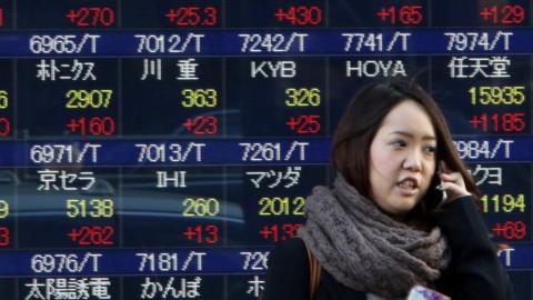 A woman passes before a share prices board in Tokyo on January 22, 2016.