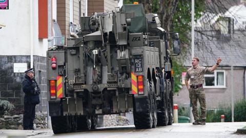 Military vehicle operating in the street with personnel directing, in Plymouth on 23 February