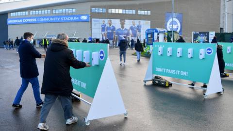 Fans wearing masks use hand sanitisers outside Brighton's Amex Stadium