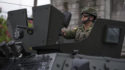 A man in military uniform drives a black armoured vehicle