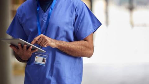 medical worker dressed in blue scrubs holding a digital tablet