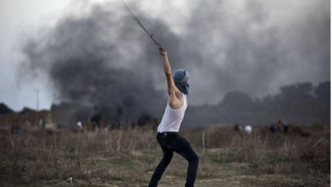 A Palestinian protester uses a slingshot to throw stones towards Israeli soldiers during clashes near the border fence between Israel and the central Gaza Strip east of Bureij on 15 October 2015.