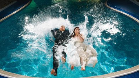 Louise Young and Sam Gilbert jumping into a swimming pool on their wedding day