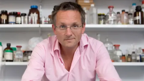 An image showing Michael Mosley in front of chemicals in bottles