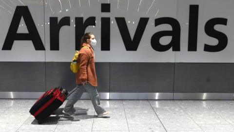 Woman in front of arrivals sign at Heathrow Airport.