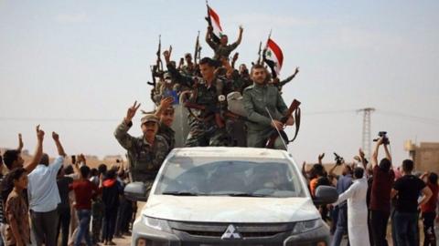 Syrian government forces wave national flags as they enter the northern town of Ain Issa