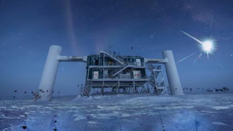 The IceCube facility, a structure built atop the ice in Antarctica. The picture is taken at nighttime, the moon a bright glow in the sky