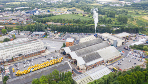 Aerial shot of Swindon's Waterside Park with various buildings, yellow lorries and a chimney with smoke emitting. 
