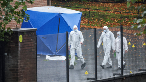 Forensics officers outside the synagogue where the attack took place, dressed in white suits close to a blue tent