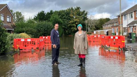 Layla Moran and an unknown resident stood in the middle of a flooded street. There are houses either side, and the water level is reasonably low (only just over shoe sole level).