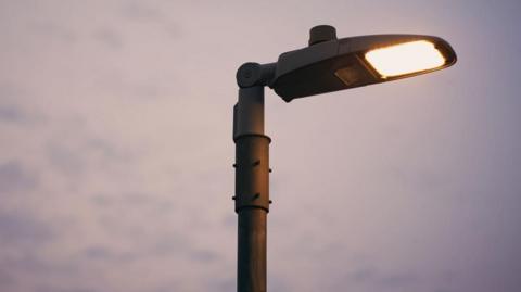 The top of a streetlight against a cloudy sky.
