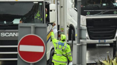 A police officer checks the paperwork of a lorry driver at a port border. 