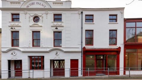 A view of the white Picture Palace from the street with its red doors and windows