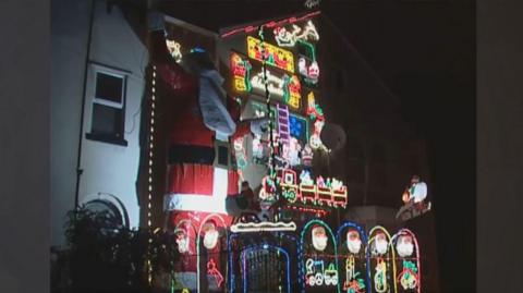 A three storey house decorated in Christmas lights with a giant Father Christmas