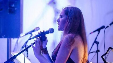 Alexis Wade singing into a microphone on a purple-lit stage