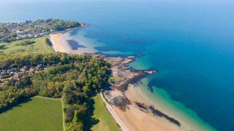 Aerial shot of Helen's Bay beach, showing sand, water and greenery.