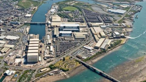 An aerial view of BAE Systems, Barrow. There are lots of buildings and car parks constructed on a peninsula surrounded by sea.