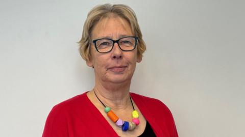 A woman in a red cardigan with a multicoloured beaded necklace