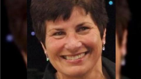A close-up image of Valerie Freer smiling with short dark hair and earrings.