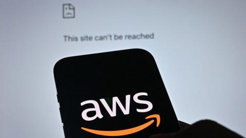 The white and orange Amazon Web Services (AWS) logo displayed on the black screen of a smartphone. In the background is a Google Chrome web page displaying an error message: "This site can't be reached."