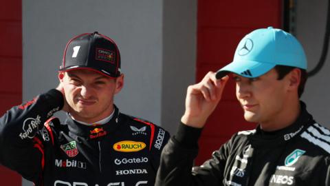 Max Verstappen scrunches up his face while stood next to George Russell, who is adjusting his cap, at the Emilia-Romagna Grand Prix at Imola in May 2025