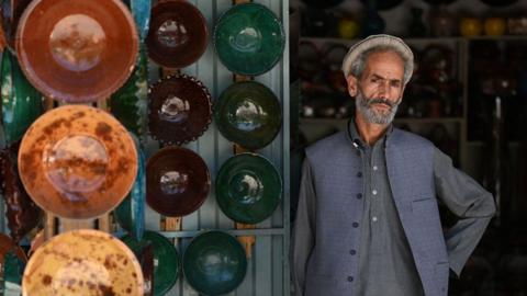 An Afghan man with his plates outside his shop