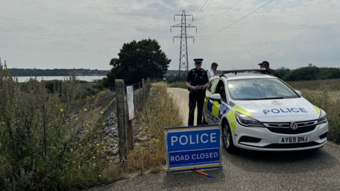 Police standing by a police car which has a "Police Road Closed" sign beside it